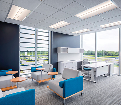 AT3 recessed troffers in a grid ceiling lighting a modern office space with a white desk and blue and gray chairs in a sitting area.