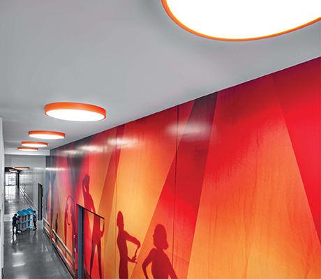 Surface mount orange RND round fixtures lighting a corridor with an orange mural along the wall showing people dancing.