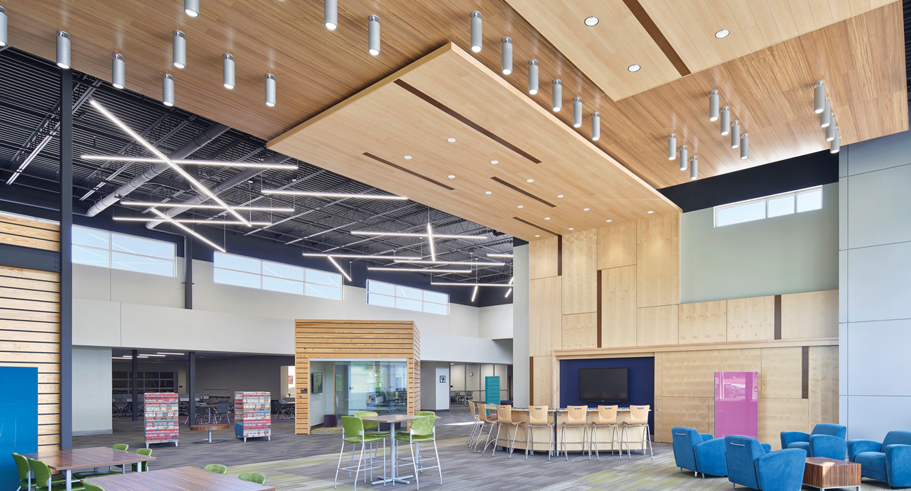 Modern educational facility lobby with high ceilings and surface mount cylinders, suspended continuous, and downlight product.